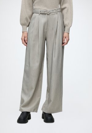 Pantalon gris taille haute à jambes larges avec de fines rayures, ceinturé à la taille, porté avec un pull beige et des chaussures plateformes noires épaisses.