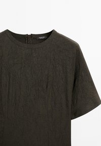 Dunkelgrünes, zerknittertes Stoffoberteil mit Rundhalsausschnitt und kurzen Ärmeln. Verfügt über einen Reißverschlussverschluss hinten. Einfaches, geschmackvolles Design.