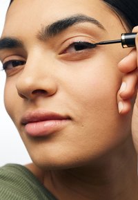 Applicateur d'eyeliner liquide noir avec un accent doré, appliqué le long de la paupière supérieure d'une personne avec une peau lisse et des lèvres pleines.