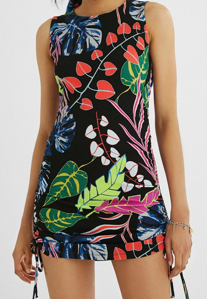Robe noire sans manches avec des motifs de feuilles tropicales colorées en vert, bleu, rouge, blanc et rose, portée par une personne avec un bracelet au poignet droit.