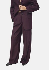 Costume bordeaux avec une veste cintrée à un bouton et un pantalon à jambes larges. Texture lisse, design minimaliste, sans motifs apparents.