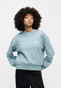 Ανοιχτό μπλε φούτερ με στρογγυλή λαιμόκοψη, χαλαρή εφαρμογή, ριμπ μανσέτες και ζώνη στην κάτω πλευρά. Διαθέτει μικρό λευκό λογότυπο στο στήθος.