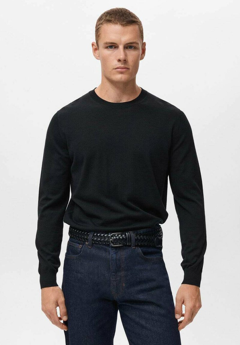 Črna pletena dolge rokave s krožnim izrezom, v kombinaciji s temno modrimi džinsom in črnim pletenim pasom. Gladka tekstura, ozek kroj.