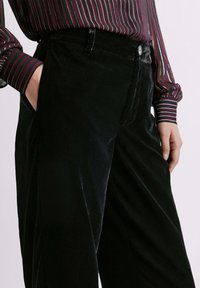 Mustardainest švuntedest, sirge lõikega püksid, millel on ees tasku ja nööp sulgemiseks. Tekstureeritud kude, millel on peen sära.