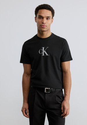 T-shirt en coton noir avec un logo "cK" blanc sur la poitrine, manches courtes et col rond classique.