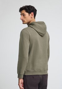 Felpa con cappuccio in verde oliva, realizzata in misto cotone, presenta maniche lunghe, polsini a costine e una vestibilità rilassata. Texture liscia, design minimale.