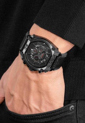 Black analog wristwatch with textured strap, large rectangular case, and multiple dials. Features red accents and knob on side for adjustments.