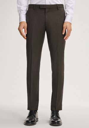 Pantalons ajustés marron foncé avec une texture lisse, présentant un design à devant plat, des passants de ceinture et une coupe fuselée, associés à des chaussures de ville noires.