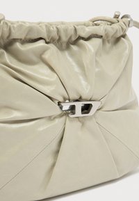 Μπεζ μαλακό δερμάτινο τσαντάκι με σούρες στο πάνω μέρος και ασημί μεταλλικό κούμπωμα στο κέντρο μπροστά.