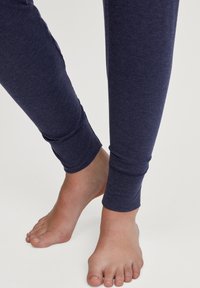 Navyblauwe leggings van zachte stof met een aansluitende pasvorm en geribde boorden, rustend boven blote voeten tegen een lichte achtergrond.
