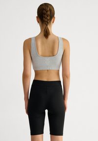 Grijze katoenen sportbeha met een ronde achterkant en een witte logodetail; gecombineerd met zwarte knielange legging van rekbaar materiaal.