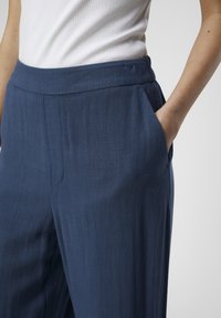 Pantalons larges bleu marine en tissu léger texturé avec une taille lisse et des poches latérales.