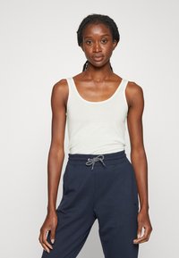 Lys grå tanktop med brede stropper, sammen med mørkeblå sweatpants med snor. Glatt tekstur, uformelt design og avslappet passform.