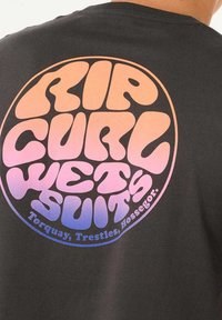 Camiseta negra con un gran gráfico redondo y multicolor en tonos degradados de rosa, púrpura y naranja con el texto "RIP CURL WETSUITS."