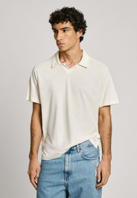 Short-sleeve polo shirt, cream-colored, lightweight fabric, with a notched collar. Paired with light blue distressed denim jeans.