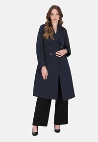 Sötétkék, dupla soros trench kabát nagy hajtókákkal és két elülső zsebbel. Fekete, bőszárú nadrággal és magassarkú cipővel párosítva.