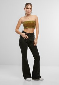 Olijfgroen strapless crop top met rode geborduurde tekst, gecombineerd met hoge zwarte flare jeans en witte sneakers.