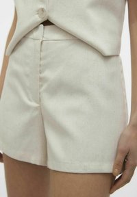 Pantaloni shorts di colore crema, realizzati in tessuto testurizzato, con un design aderente, vita media e orlo pulito.
