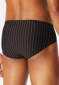 Costumi da bagno neri con strisce verticali bianche e rosse, caratterizzati da una texture liscia e una vita elastica. Modellati per adattarsi in modo aderente.