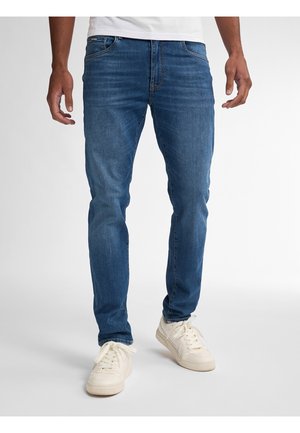 Jeans de denim azul deslavado con un diseño ajustado, cinco bolsillos y detalles de costura sutiles; combinados con zapatillas blancas.