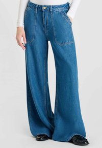 Vaqueros de denim azul de pierna ancha con cintura alta, dos bolsillos frontales y cierre de botón. La tela tiene un acabado suave y texturizado.