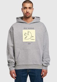 Grå hætte sweatshirt med en forlommer, der har et trykt design af en due og tekst af Picasso, lavet af blødt stof.