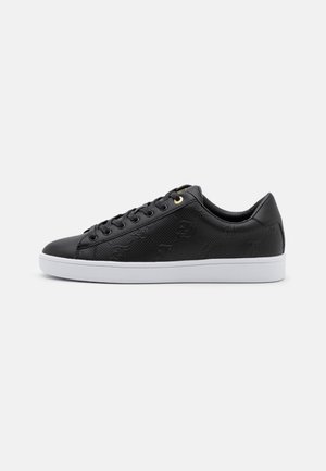 Black low-top leather sneaker with embossed patterns, black laces, gold eyelet, and a white rubber sole, shown from the outer side.