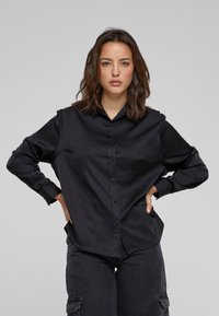 Zwarte lange mouw button-up shirt van gladde stof, met een klassieke kraag en een relaxte pasvorm. Gecombineerd met donkere cargobroeken.