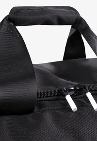 Juodas audinio maišelis su tekstūruota paviršiaus struktūra, turintis užtraukiamą angą ir du baltus užtrauktukų laikiklius. Rankenos yra trumpos ir pagamintos iš to paties medžiagos.