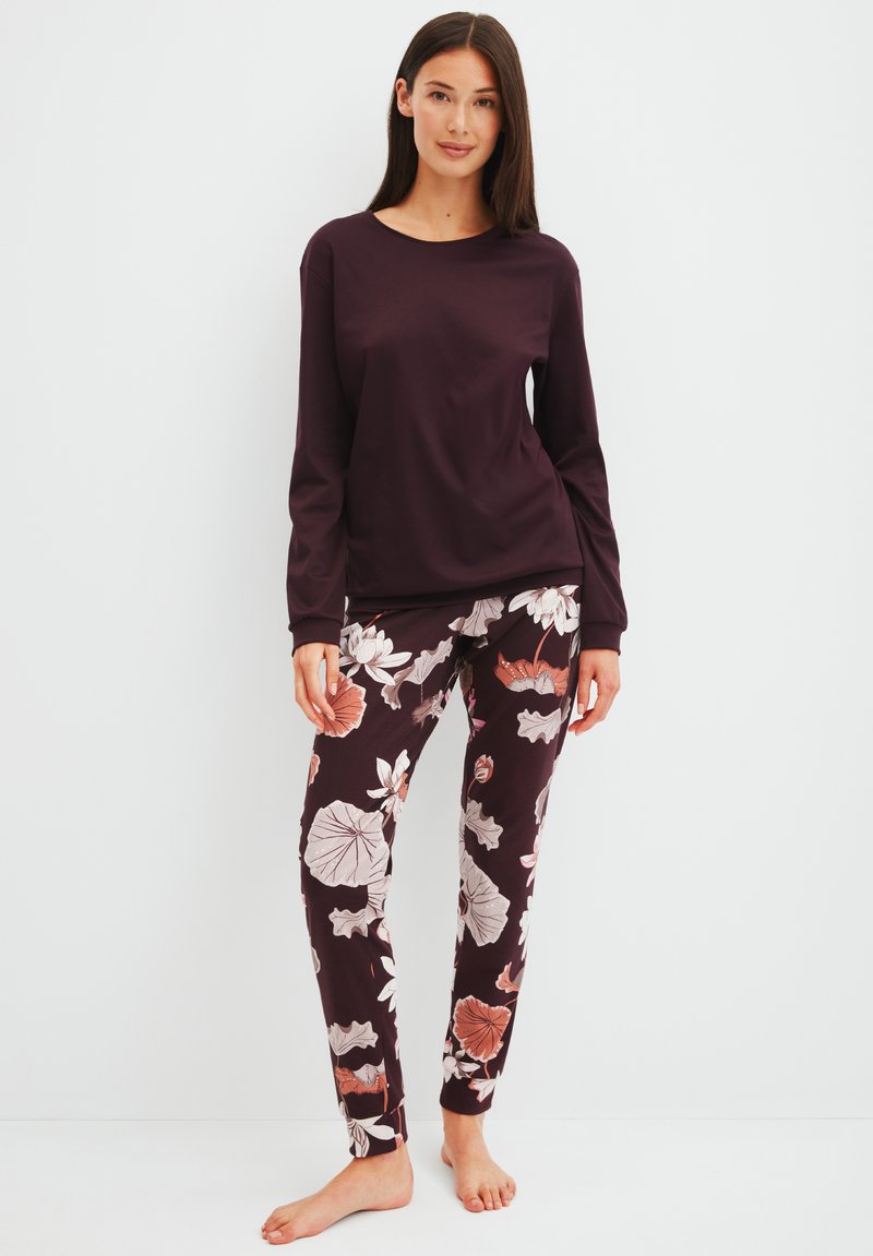 Haut à manches longues violet associé à un pantalon à motif floral comprenant des nuances de rose et de blanc sur un fond sombre. Tissu en coton doux.
