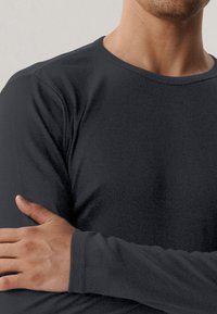 Czarna bluzka z długim rękawem z okrągłym dekoltem, wykonana z miękkiego materiału o gładkiej fakturze, z dopasowanymi rękawami i bez widocznych wzorów czy akcentów.