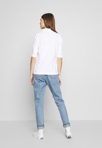 Kortermet hvit polo skjorte laget av bomull, kombinert med lyseblå denimjeans. Uformell design med oppbrettede ermer og en avslappet passform.