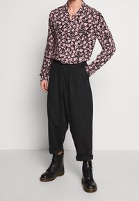 Zwart en roze bloemenprint shirt met lange mouwen en kraag, gecombineerd met zwarte, hoog getailleerde, taps toelopende broek en zwarte veterboots.