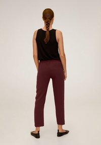 Pantalon bordeaux à coupe décontractée, jambes fuselées, taille élastique et une poche arrière unique, associé à un haut noir sans manches.