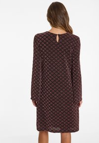 Long-sleeve dress in dark burgundy with a textured diamond pattern, featuring a keyhole back detail and a loose-fitting silhouette.