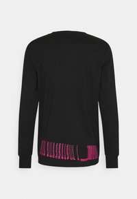 Svart långärmad tröja i mjukt material med djärv rosa text vid nederkanten, prydd med ett mönster av stiliserade linjer och ord.