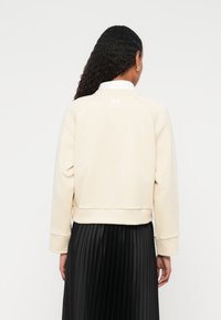 Ανοιχτό μπεζ φούτερ με απλό σχέδιο, με μανίκια ράγκλαν και ριμπ τελείωμα. Στο πίσω μέρος υπάρχει μικρή λευκή λεπτομέρεια λογότυπου.