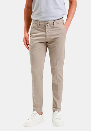 Pantaloni beige slim-fit realizzati in tessuto misto cotone, con chiusura a bottone, passanti per cintura e tasche laterali. Indossati con sneakers bianche.