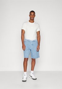 Lys grå bomull t-skjorte med rullede ermer, kombinert med blå denimshorts med elastisk midje og justerbar snor. Hvit sneakers.