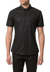 Camisa negra de manga corta y botones, hecha de una tela suave, con un cuello puntiagudo y dos bolsillos en el pecho, exhibida en un modelo.