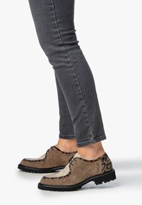 Scarpe in pelle con lacci caratterizzate da un mix di materiali marroni testurizzati e stampa leopardata, con una suola nera robusta. Abbinati a jeans skinny grigi.
