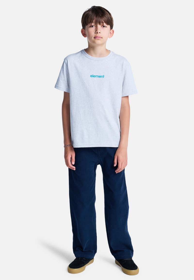 Chłopiec stojący przodem, ubrany w jasnoszary t-shirt "element", granatowe spodnie, czarne buty oraz plecioną bransoletkę na lewej ręce.