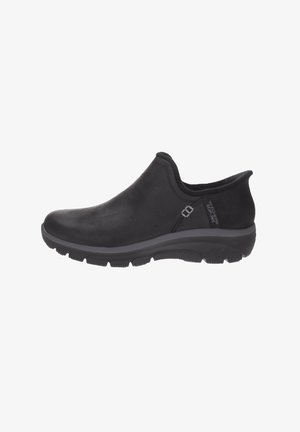 Zapato negro tipo slip-on con suela acolchada, punta redondeada y tacón bajo, con etiqueta lateral que dice "Skechers Slip-Ins."