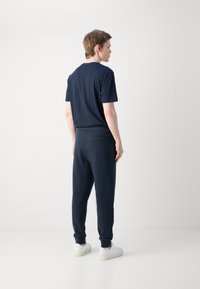 Námornícko modré bavlnené tričko a zodpovedajúce teplákové nohavice, ktoré majú voľný strih, elastický pás a minimalistický dizajn. Biele tenisky dopĺňajú outfit.