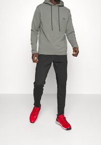 Grå långärmad hoodie med dragband, svarta byxor och ljusröda träningsskor. Outfitten har en minimalistisk design och kontrasterande färger.