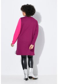 Robe à manches longues avec un corps violet et des manches roses, en tissu doux. Associée à des leggings noirs brillants et des bottines argentées.