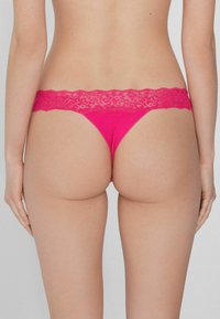 Rosa Tanga mit einem breiten, floralen Spitzenbund. Verfügt über eine glatte Oberfläche und minimale Abdeckung hinten.