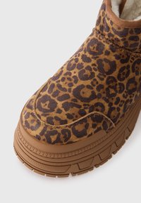 Bota de suela gruesa marrón con parte superior de print de leopardo y forro de borreguito visible en el collar del tobillo.