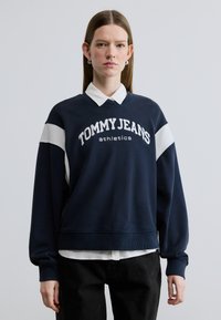 Φούτερ σε ναυτικό μπλε με το λευκό κείμενο "TOMMY JEANS athletics", διακοσμημένο με λευκές ρίγες στα μανίκια και ριμπ μανσέτες.
