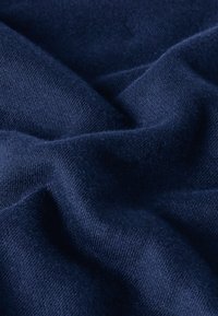 Tejido azul marino con una textura suave y un ligero brillo, que muestra intrincados patrones de punto y suaves pliegues, asemejando un material ligero.